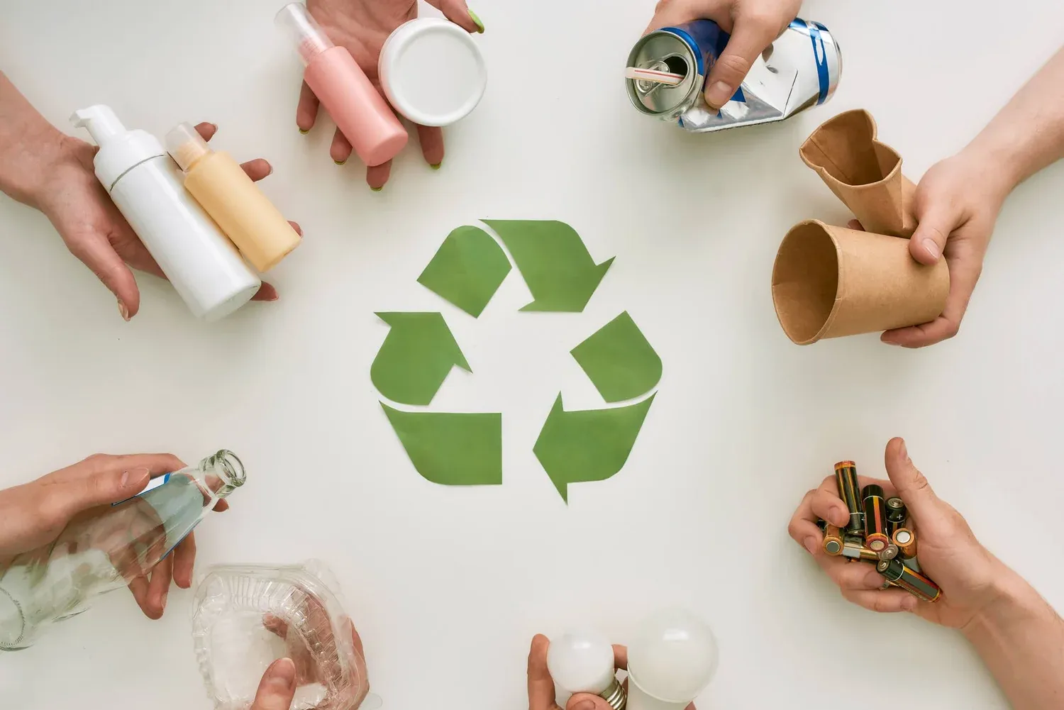 Hands holding recyclable items around a recycling symbol